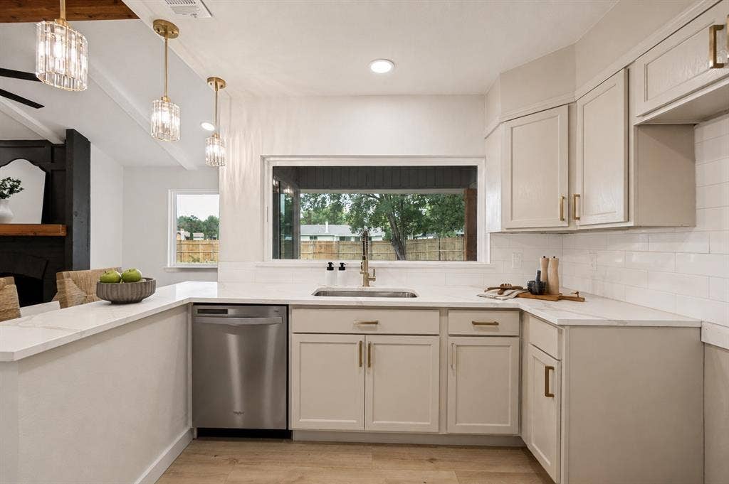 641 Stroud Lane, Garland, TX 75043 Kitchen featuring light-toned cabinetry with brass hardware, a stainless steel dishwasher, white subway tile backsplash, and light-toned countertops