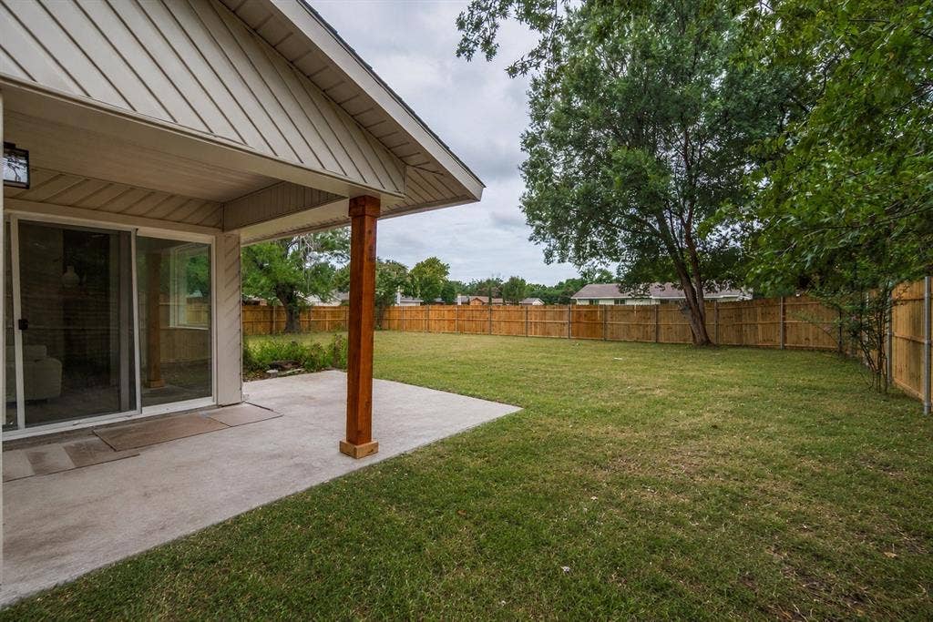 641 Stroud Lane, Garland, TX 75043 Rear exterior patio with a wood-finished support column, a sliding glass door, and a full wood privacy fence surrounding a grassy yard