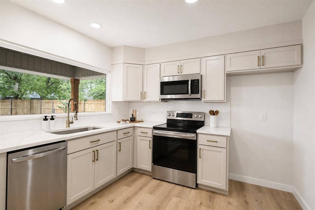 641 Stroud Lane, Garland, TX 75043 Contemporary kitchen featuring light wood-finish flooring, white shaker-style cabinetry with gold-tone hardware, stainless steel appliances, white subway tile backsplash, and a large window above the sink
