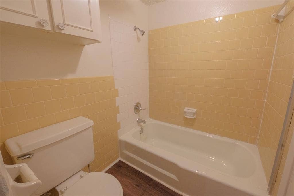 6317 Granbury Road, #6321, Fort Worth, TX 76133 Bathroom featuring a ceramic bathtub, yellow subway tile surround, white wall tile, wood-finish flooring, and white cabinetry with decorative knobs