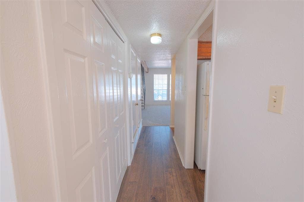 6317 Granbury Road, #6321, Fort Worth, TX 76133 Hallway featuring wood-finish flooring, white paneled bifold closet doors, a flush-mount ceiling light fixture, and white painted walls