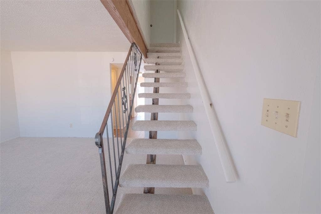 6317 Granbury Road, #6321, Fort Worth, TX 76133 Carpeted staircase with an ornamental metal railing and wood-finish beam