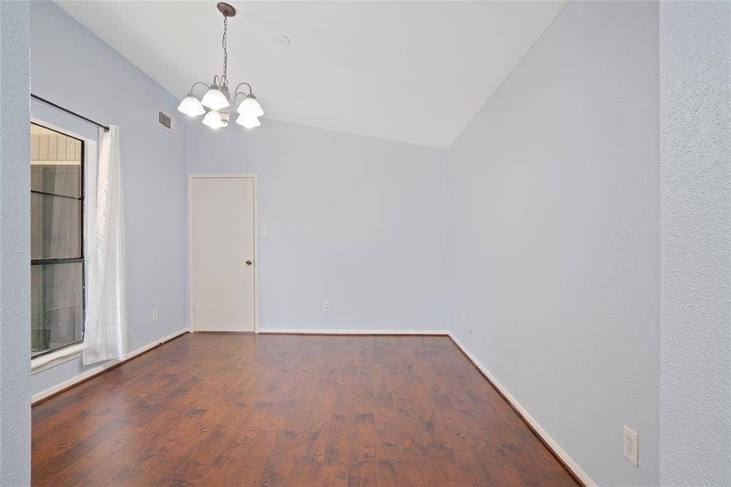 8100 Cambridge Street, #124, Houston, TX 77054 Spacious room featuring wood-finish flooring, light blue wall paint, a vaulted ceiling, and a multi-light chandelier