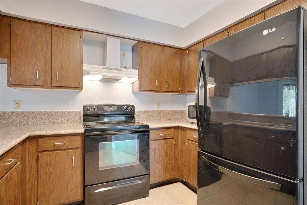 8100 Cambridge Street, #124, Houston, TX 77054 Kitchen featuring wood-finish cabinetry, speckled countertops, black electric range with overhead ventilation, and a black refrigerator