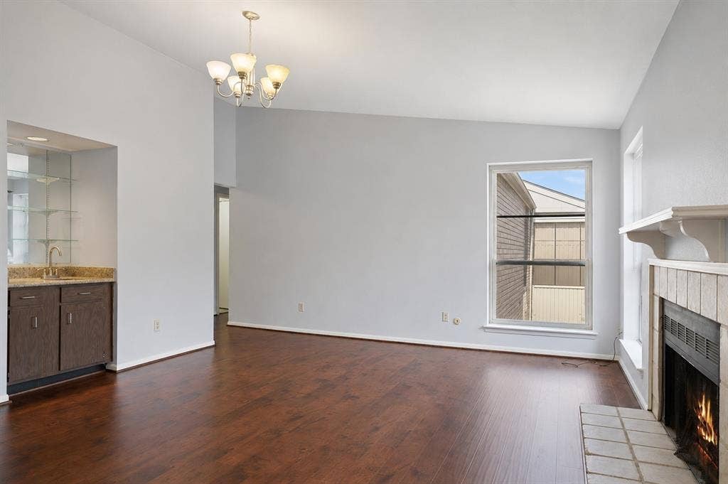 8100 Cambridge Street, #124, Houston, TX 77054 Open living area featuring wood-finish flooring, a built-in wet bar with a granite-style countertop, and a fireplace with a tiled hearth and mantle