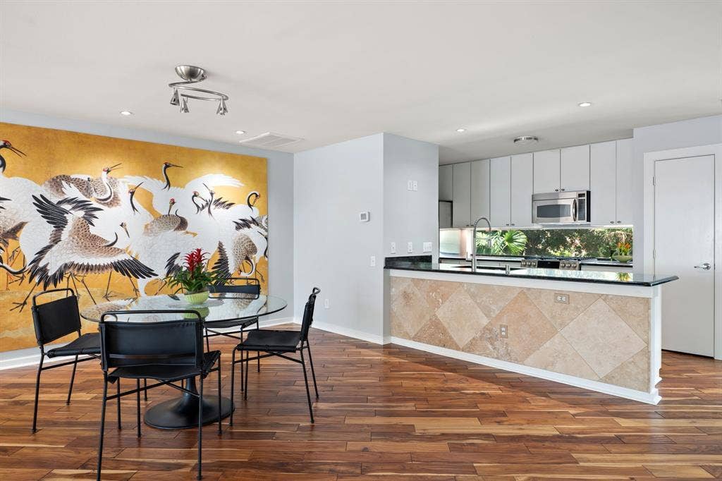 Open-concept living space featuring wood-finish flooring, a kitchen island with stone tile facing and a black countertop, modern white kitchen cabinetry, and recessed lighting
