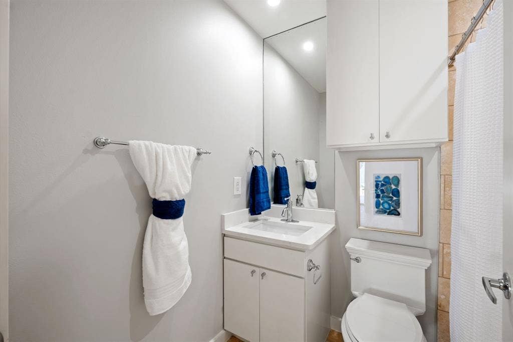 Bathroom featuring a vanity with a white countertop and undermount sink, a large wall-mounted mirror, white cabinetry, and a toilet