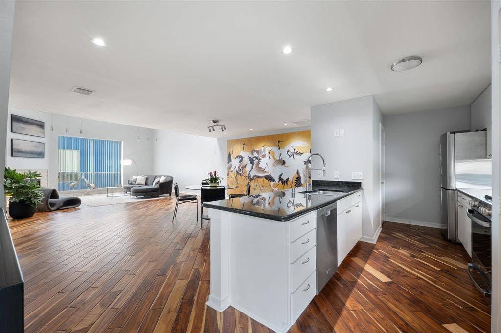 Open-concept living space featuring wood-finish flooring, recessed lighting, and a kitchen island with a dark countertop and integrated sink