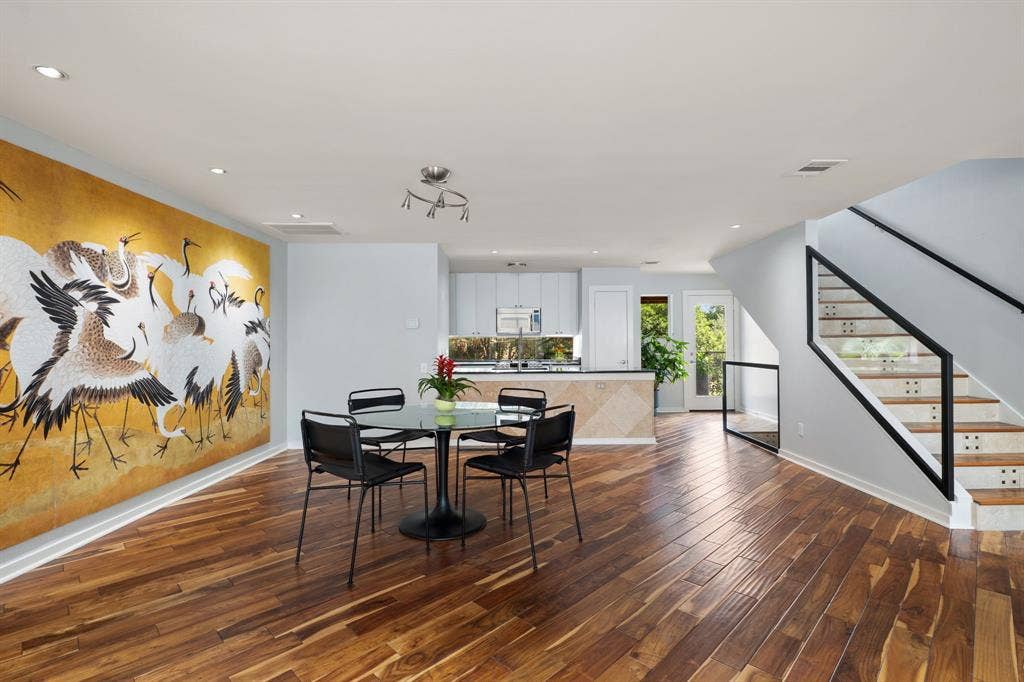 Open-concept living area with rich wood-finish flooring, recessed lighting, and a modern staircase featuring black metal railings