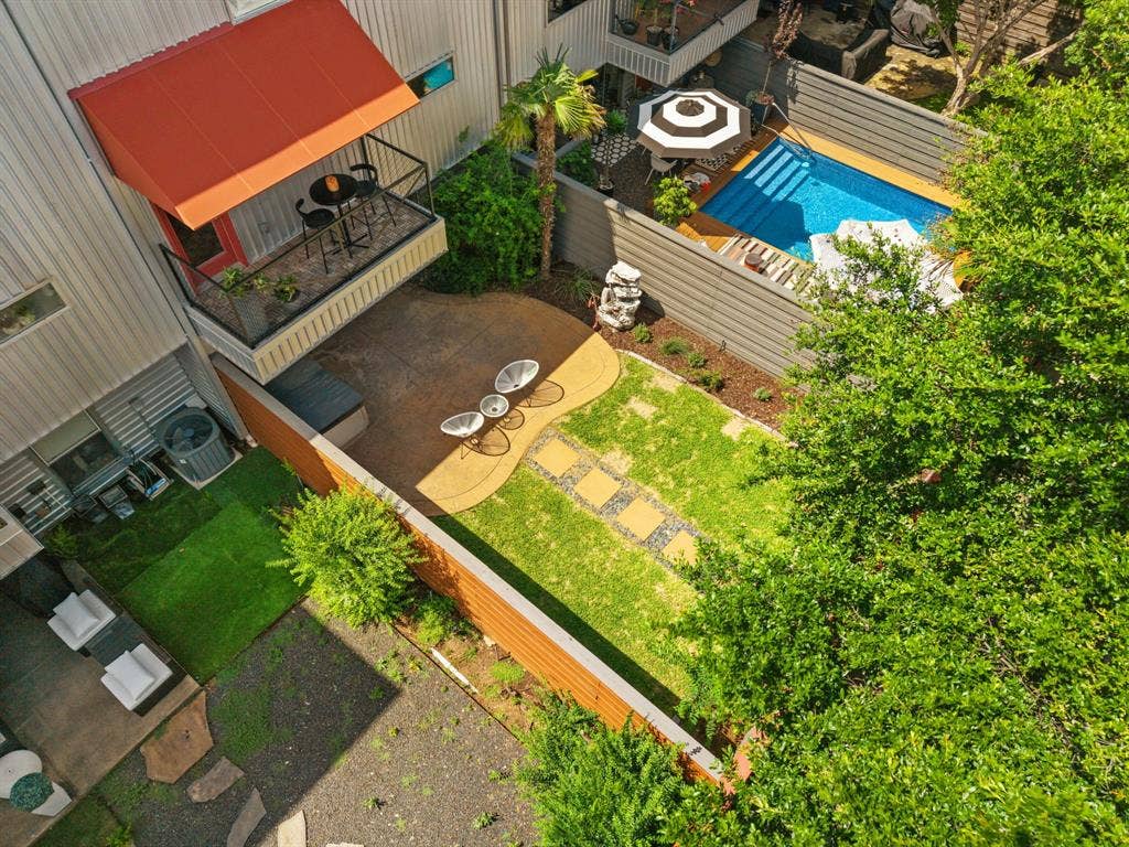 Private outdoor space featuring a rectangular pool, manicured lawn with stepping stones, an upper-level balcony with an awning, and perimeter fencing