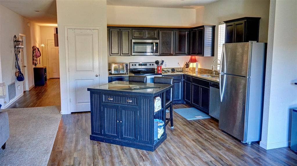 741 Windsor Court, Lavon, TX 75166 Kitchen featuring wood-finish flooring, dark cabinetry, stainless steel appliances, and a central island with a contrasting dark finish