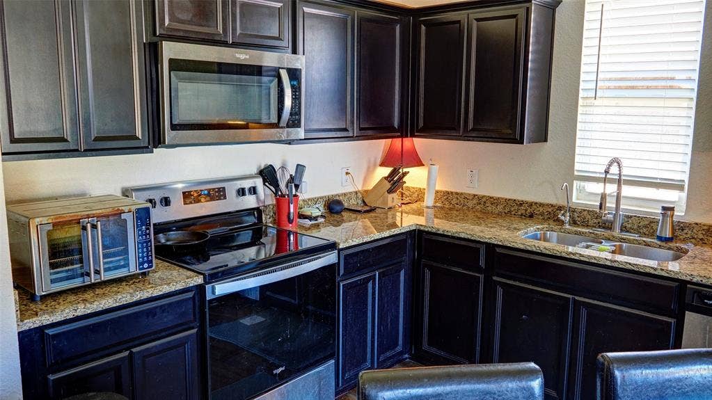 741 Windsor Court, Lavon, TX 75166 Kitchen featuring dark cabinetry, granite-style countertops, stainless steel appliances, and a double basin sink with a gooseneck faucet