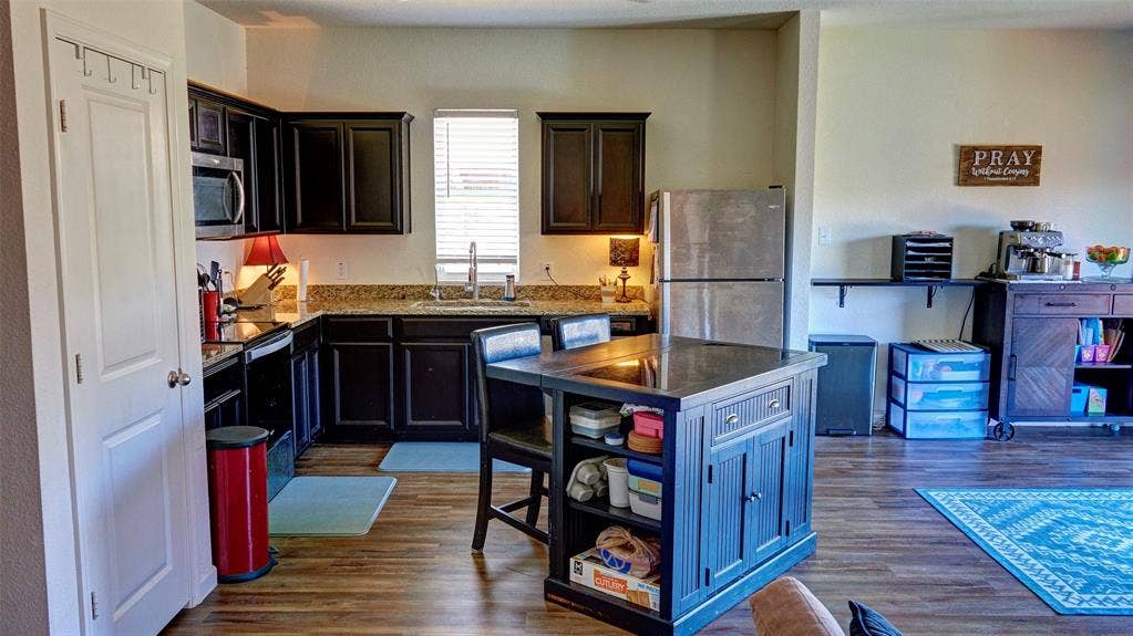 741 Windsor Court, Lavon, TX 75166 Kitchen featuring dark wood cabinetry, a central island with seating, stainless steel appliances, granite countertops, and wood-finish flooring