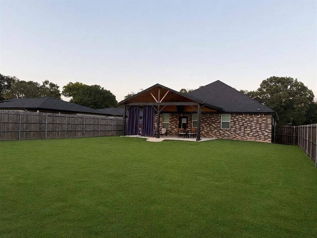 600 Lucas Drive, Athens, TX 75751 Expansive backyard featuring a manicured lawn, full privacy fencing, and a covered patio with exposed wood beams