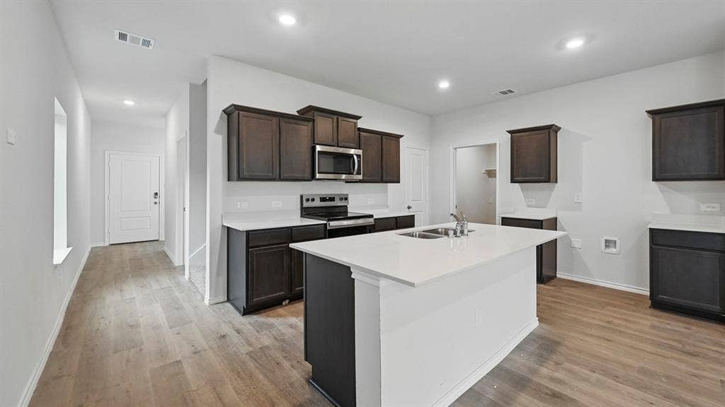5602 Gannet Place, Crandall, TX 75114 Contemporary kitchen featuring a central island with a double basin sink, dark wood-finish cabinetry, light-toned countertops, and stainless steel appliances