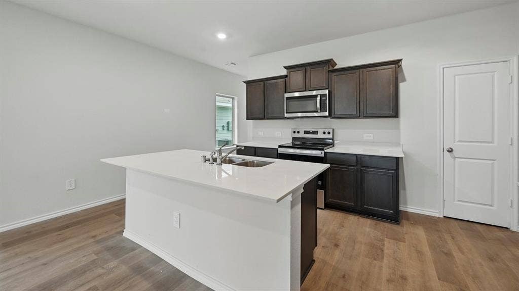 5602 Gannet Place, Crandall, TX 75114 Modern kitchen featuring an island with an undermount sink, dark wood cabinetry, stainless steel appliances, and wood-finish flooring