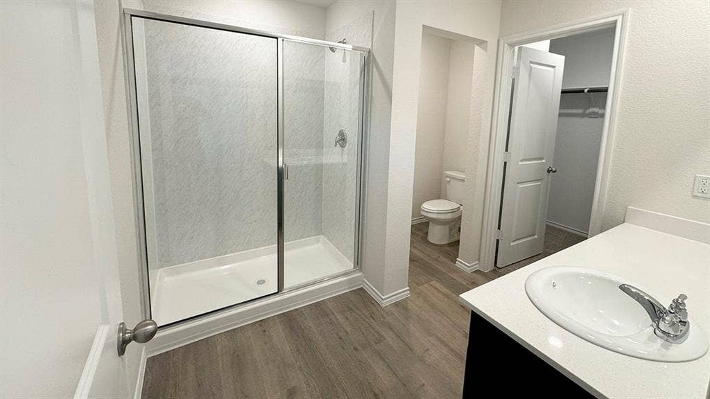 5004 Shumard Drive, Lindale, TX 75771 Bathroom featuring a glass-enclosed shower, white vanity with an undermount sink, quartz-finish countertop, and wood-finish flooring