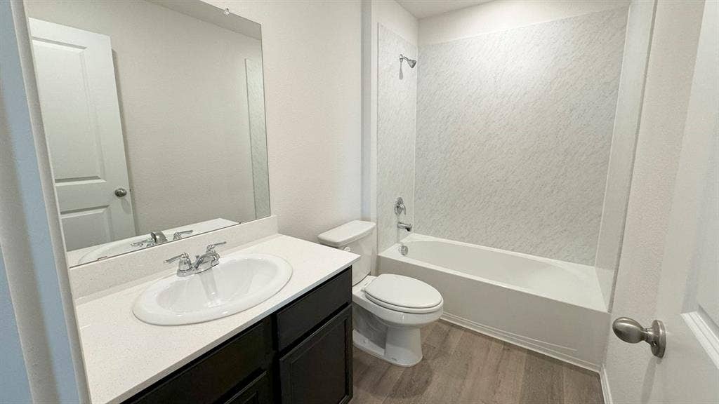 5004 Shumard Drive, Lindale, TX 75771 Bathroom featuring a white bathtub with a textured surround, a dark wood-finish vanity with a white countertop and integrated sink, and wood-finish flooring