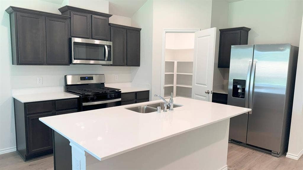 5004 Shumard Drive, Lindale, TX 75771 Modern kitchen featuring dark wood-finish cabinetry, stainless steel appliances, white countertops, and a central island with a double sink