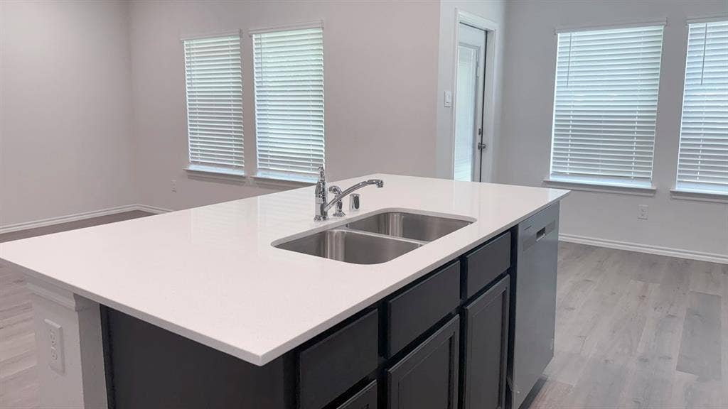 5004 Shumard Drive, Lindale, TX 75771 Kitchen island featuring a white countertop with an undermount double-basin stainless steel sink and a chrome faucet