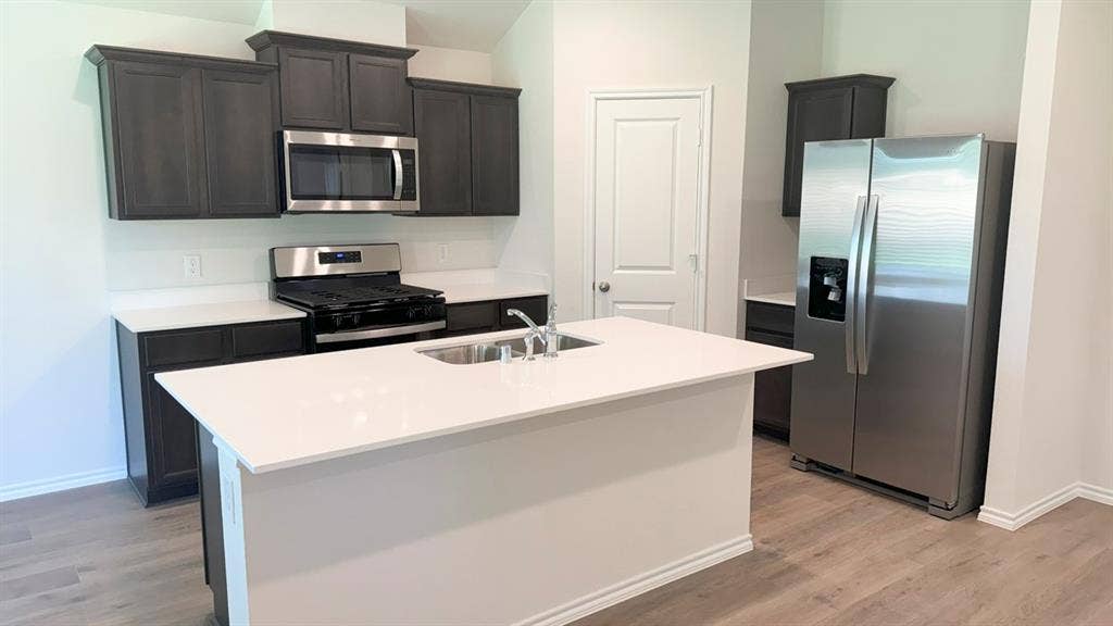 5004 Shumard Drive, Lindale, TX 75771 Kitchen featuring a central island with an integrated sink, dark wood-finish cabinetry, stainless steel appliances, white countertops, and wood-finish flooring