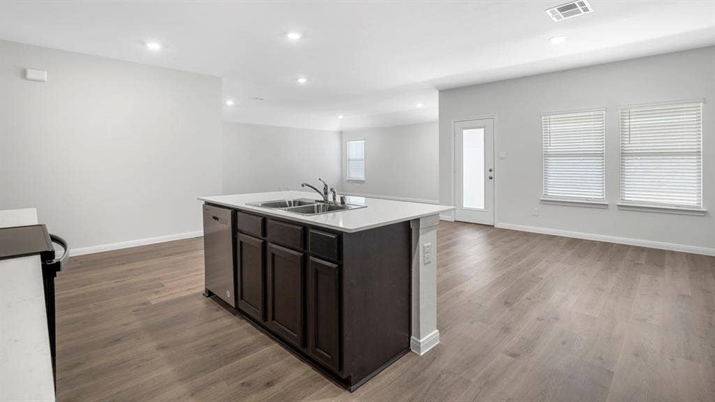 151 Arion Road, Waxahachie, TX 75165 Kitchen island featuring a dual basin sink with stainless steel appliances, dark wood cabinetry, and a light-toned countertop