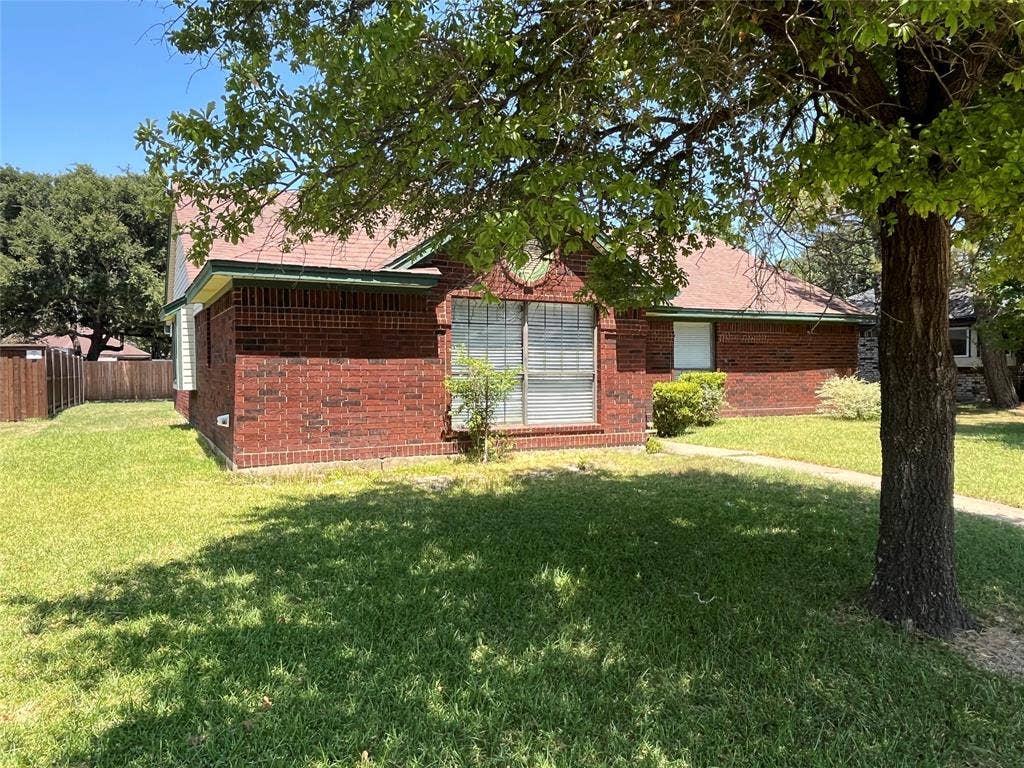 2405 Brookside Drive, Rowlett, TX 75088 Red brick exterior with a pitched roof, front-facing window, and established perimeter fencing