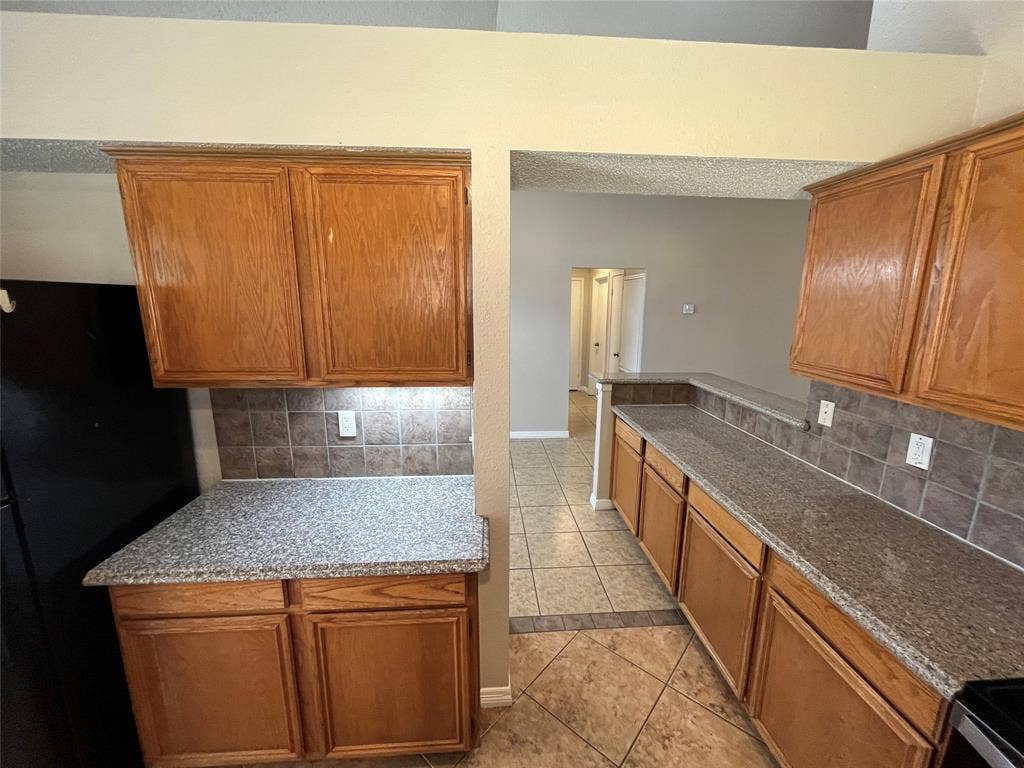 2405 Brookside Drive, Rowlett, TX 75088 Wood-finish cabinetry, speckled countertops, tile backsplash, and tile flooring