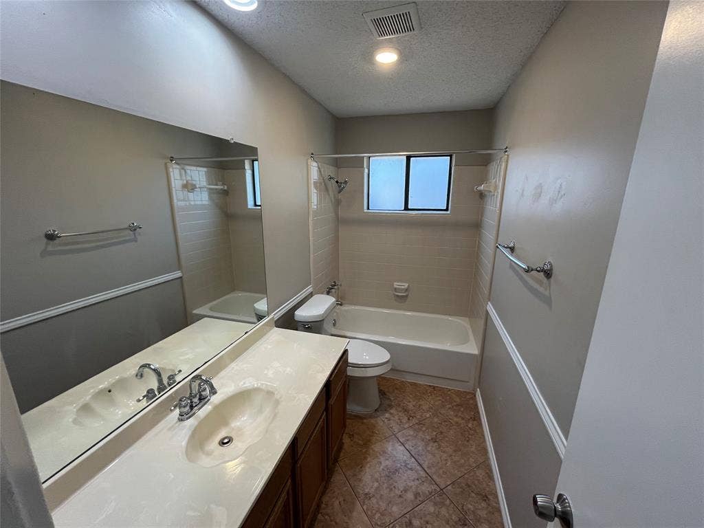 2405 Brookside Drive, Rowlett, TX 75088 Bathroom featuring a vanity with an integrated sink, a rectangular mirror, a bathtub with a tiled surround, and a fixed window
