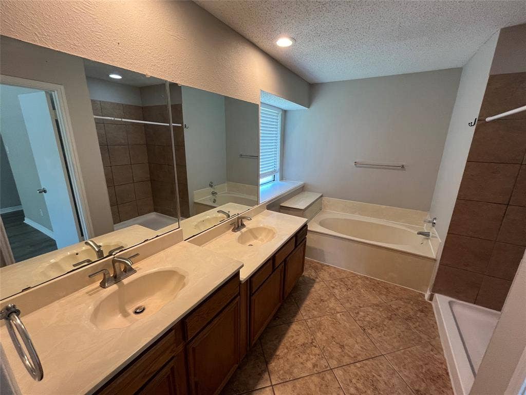 2405 Brookside Drive, Rowlett, TX 75088 Dual vanity with integrated sinks and brushed nickel fixtures, large mirror, recessed lighting, tile flooring, and a built-in bathtub