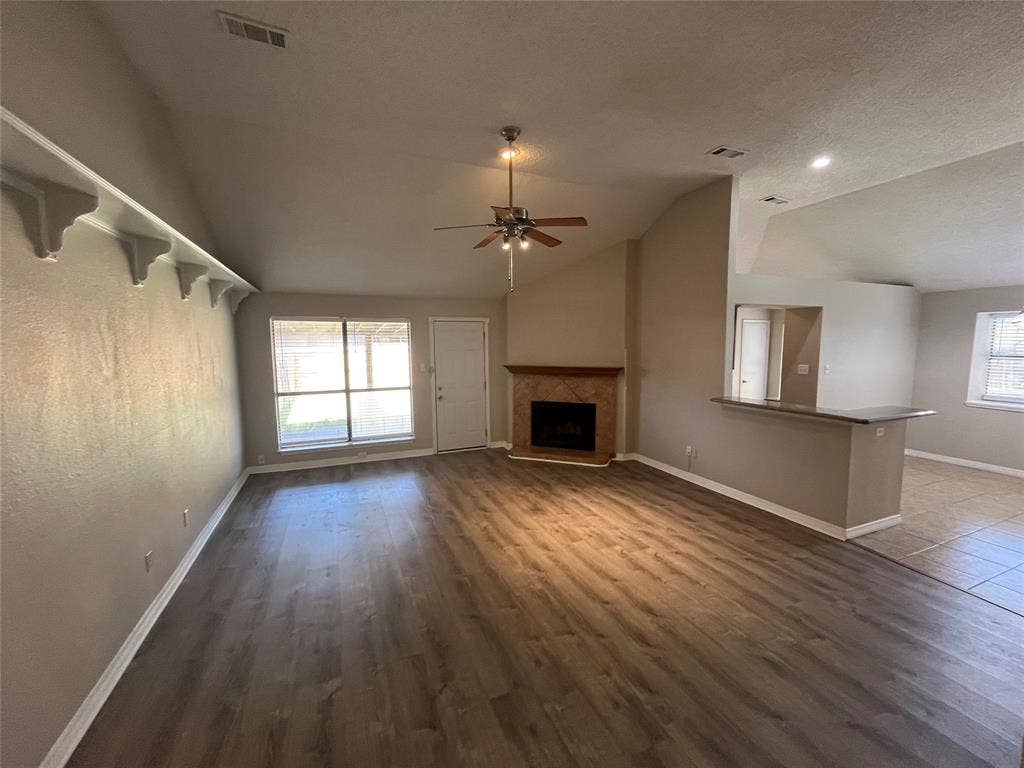 2405 Brookside Drive, Rowlett, TX 75088 Spacious living area featuring wood-finish flooring, a fireplace with a tile surround and wood mantle, and an integrated breakfast bar with a dark countertop