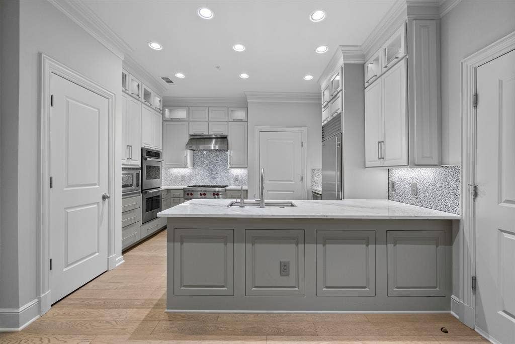 4240 Prescott Avenue, #8B, Dallas, TX 75219 Gourmet kitchen featuring a central island with a sink, light wood-finish flooring, recessed lighting, and stainless steel appliances, including a range hood and double ovens