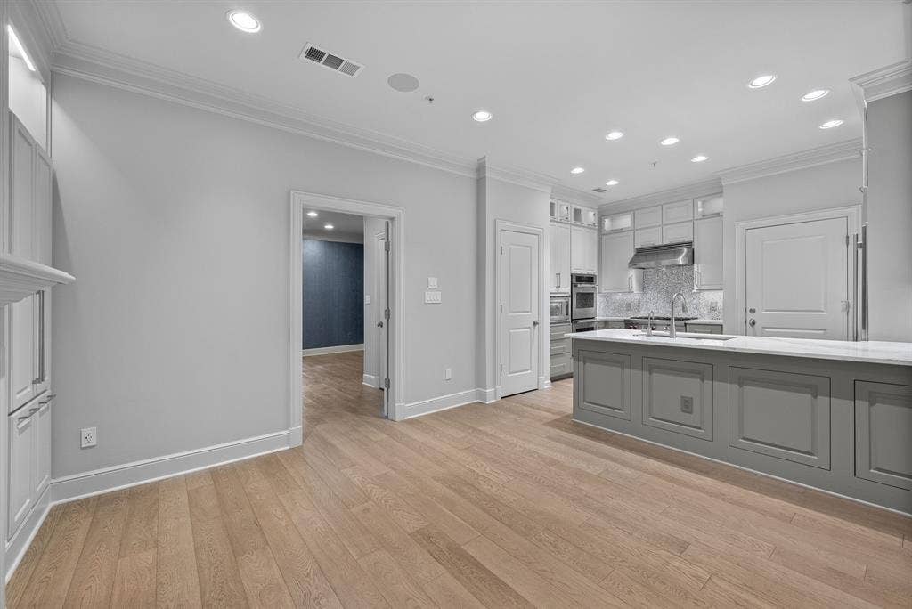 4240 Prescott Avenue, #8B, Dallas, TX 75219 Open-concept kitchen featuring an oversized island with panel detailing, light wood-finish flooring, recessed lighting, and a built-in stainless steel oven and microwave