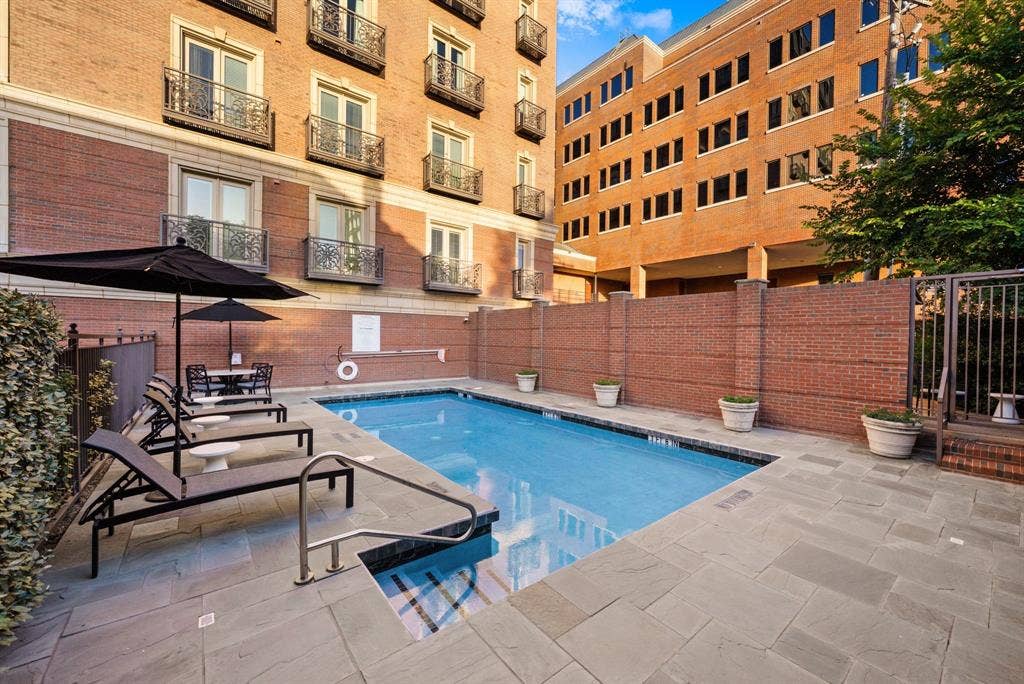 4240 Prescott Avenue, #8B, Dallas, TX 75219 Outdoor swimming pool area featuring a perimeter of large format paver stones, a brick privacy wall, and a stainless steel pool railing