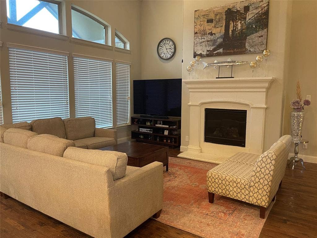 Living area featuring wood-finish flooring, a white mantel fireplace, and large windows with privacy blinds