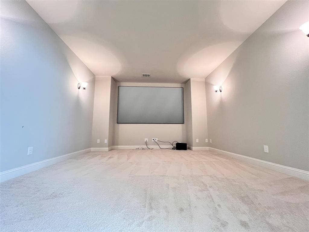 Dedicated media room featuring a large projection screen, recessed ceiling, soft carpet flooring, and wall-mounted sconces