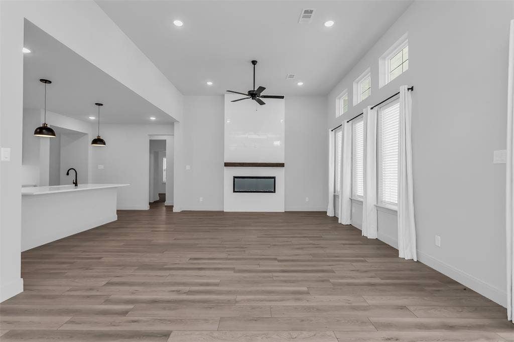 1031 Rylan Street, Midlothian, TX 76065 Spacious living area featuring wood-finish flooring, a modern fireplace with a wood mantle, and a ceiling fan