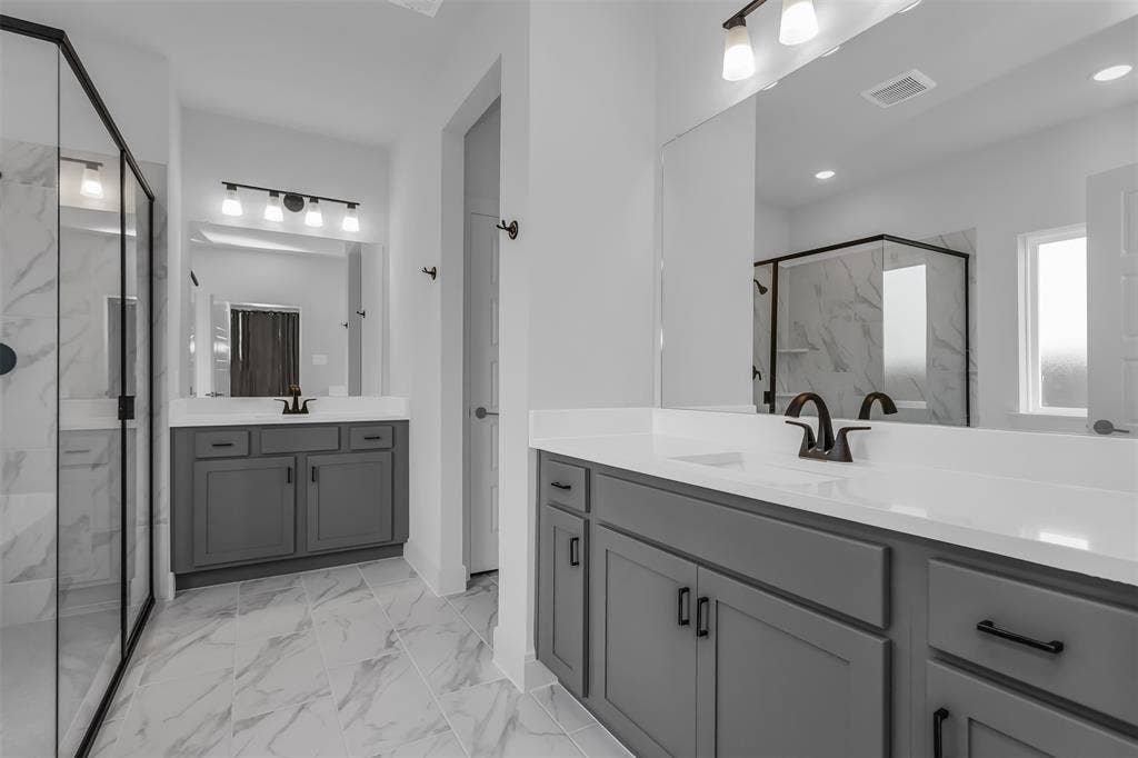 1031 Rylan Street, Midlothian, TX 76065 Double vanity bathroom featuring gray cabinetry, white countertops, black hardware, a frameless glass shower enclosure, and large-format tile flooring