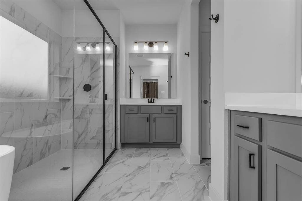 1031 Rylan Street, Midlothian, TX 76065 Spacious bathroom featuring a glass-enclosed shower with black trim, a freestanding bathtub, and white marble-look wall and floor tiling