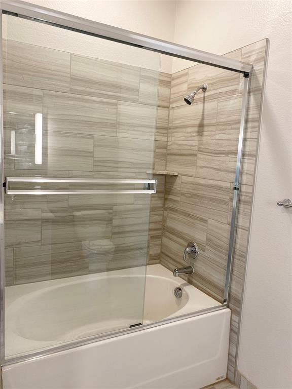 1514 E 15th Street, #10, Plano, TX 75074 Bathtub with a glass sliding enclosure, textured tile surround, chrome fixtures, and a built-in shower niche