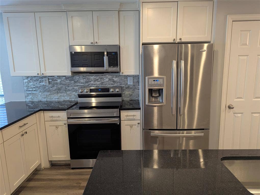 509 Pine Trail Drive, Allen, TX 75002 White shaker cabinetry, dark countertops, full suite of stainless steel appliances, stacked stone backsplash, and wood-finish flooring