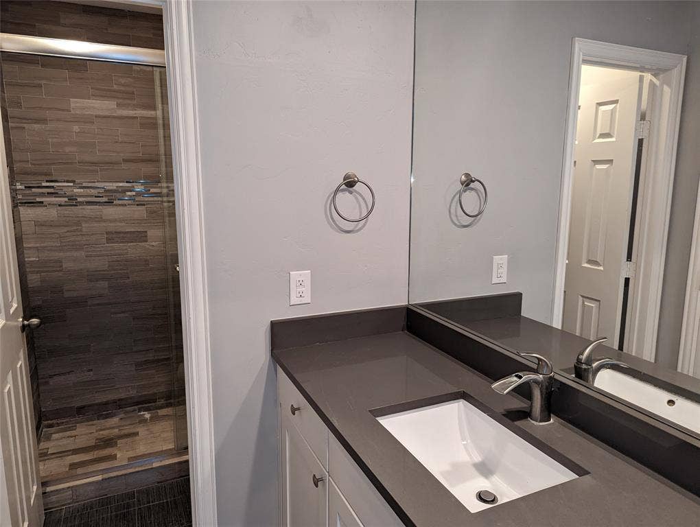 509 Pine Trail Drive, Allen, TX 75002 Modern bathroom vanity featuring an undermount sink, a sleek single-handle faucet, a dark countertop, white shaker-style cabinetry, and a full-width mirror