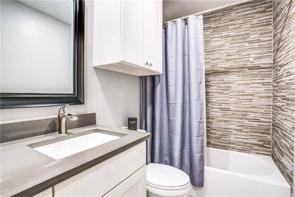 509 Pine Trail Drive, Allen, TX 75002 Bathroom featuring a built-in tub with textured tile surround, a white vanity with integrated sink and gray countertop, brushed nickel faucet, and overhead cabinetry