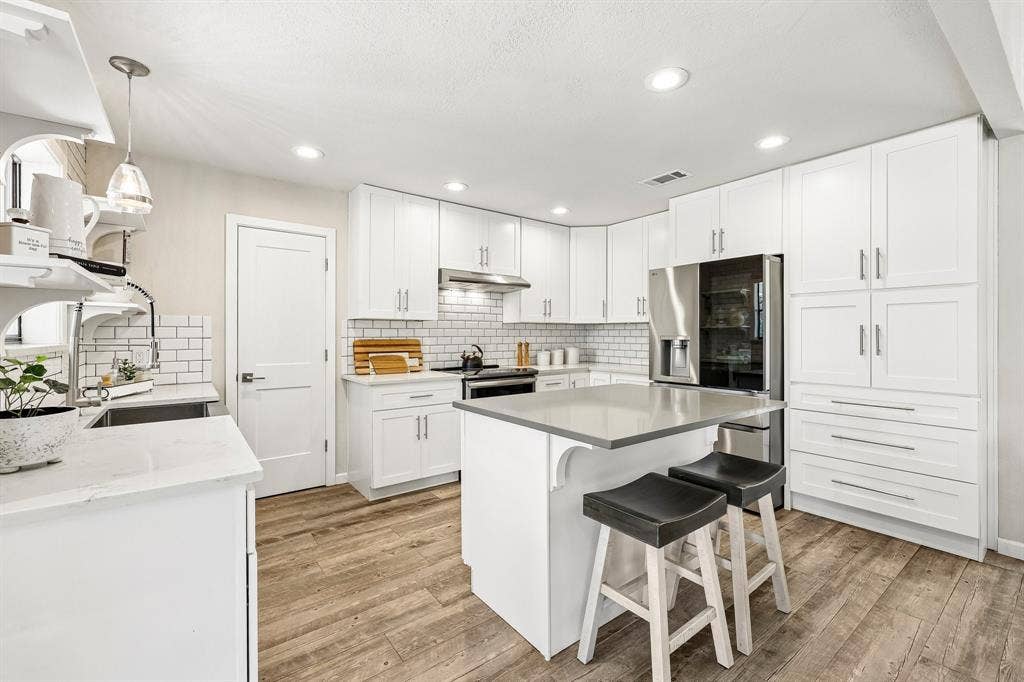 711 Bandit Trail, Keller, TX 76248 Modern kitchen featuring white shaker cabinetry, stainless steel appliances, a center island with counter seating, subway tile backsplash, and wood-finish flooring