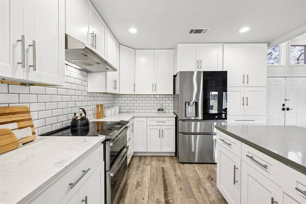 711 Bandit Trail, Keller, TX 76248 White shaker cabinetry with brushed nickel hardware, stainless steel appliances, white subway tile backsplash, light-toned countertops, and wood-finish flooring