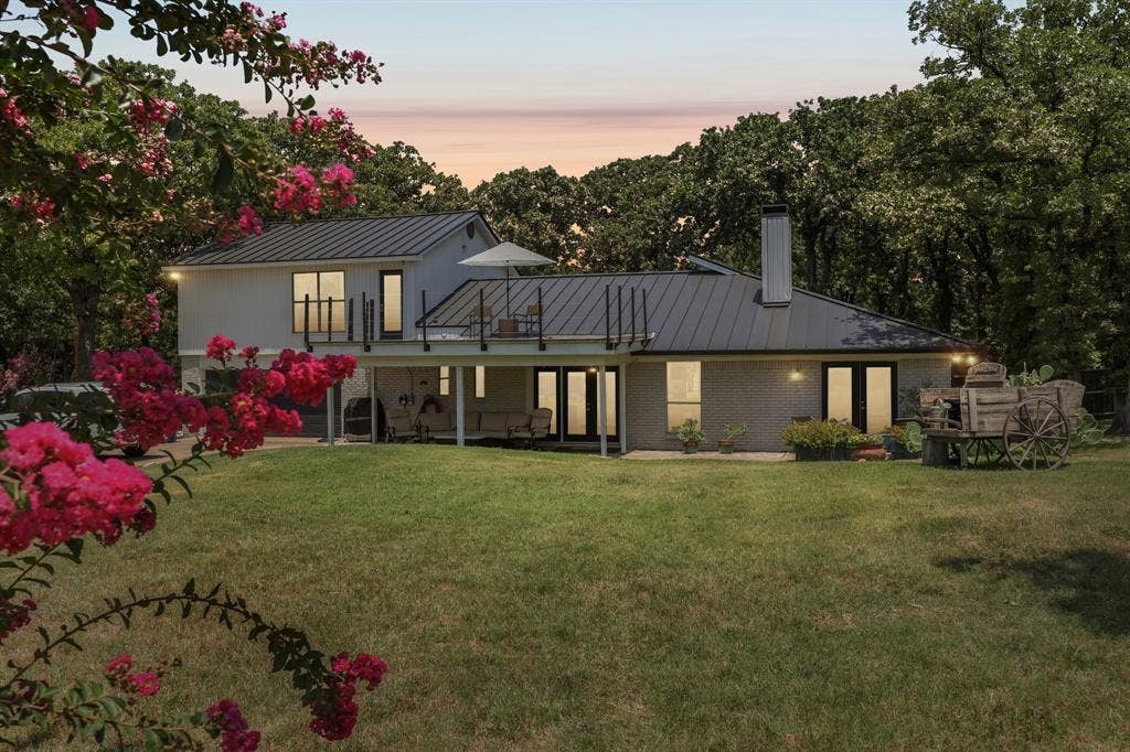 711 Bandit Trail, Keller, TX 76248 Expansive green lawn with mature trees and a multi-level home featuring a metal roof, upper-level deck with metal railings, and a covered lower patio