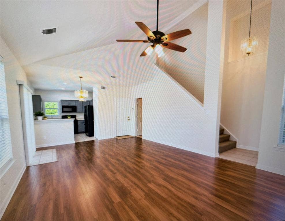 Spacious living area featuring wood-finish flooring, vaulted ceilings, and a ceiling fan with integrated lighting