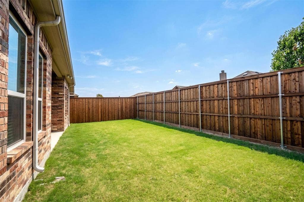 Expansive grassy yard with a full-height wood plank privacy fence featuring metal posts
