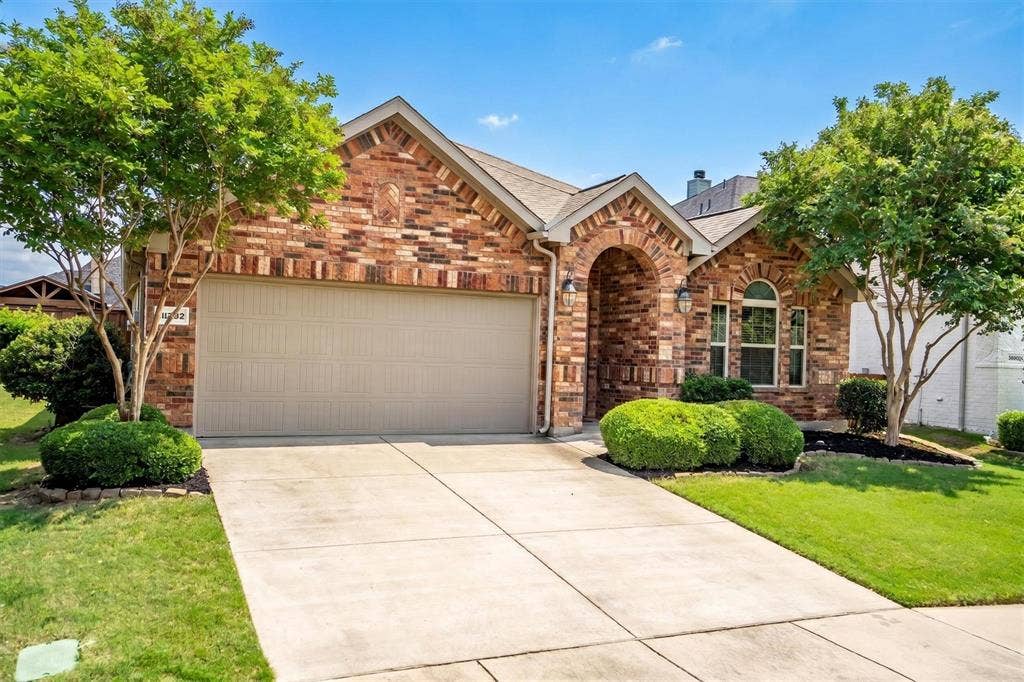 Brick exterior featuring an arched entry, a two-car garage, and mature landscaping