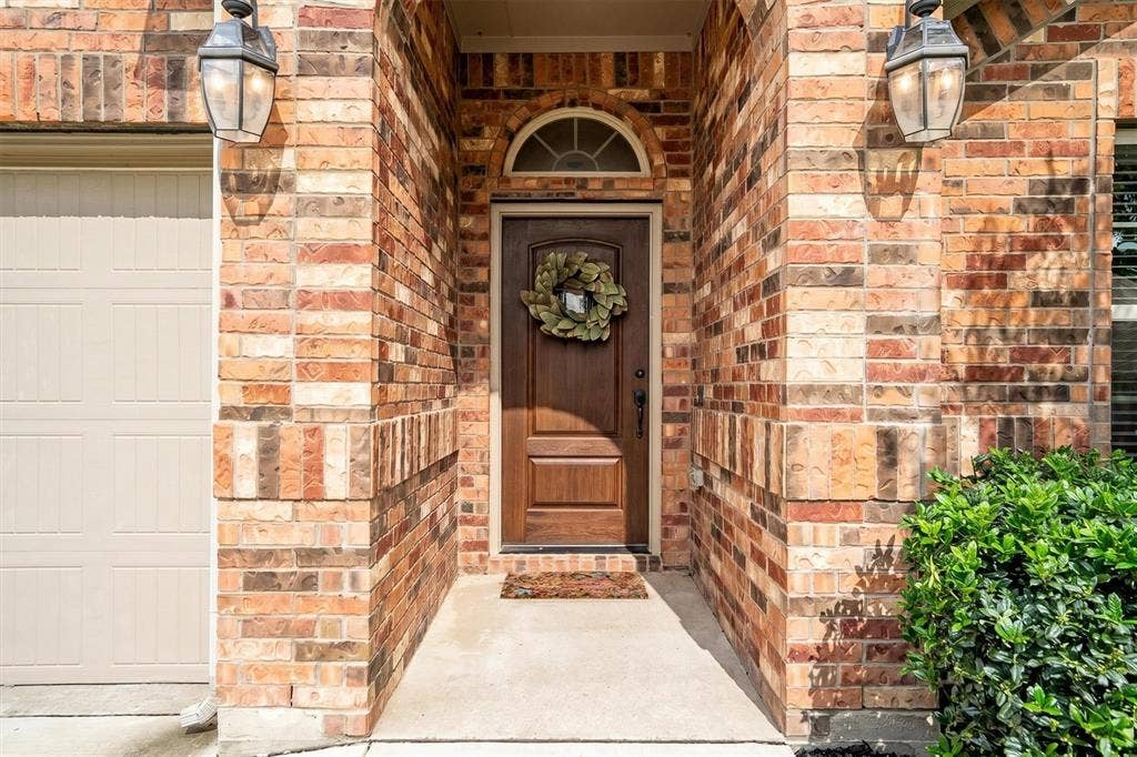 Brick exterior featuring a paneled wood-finish front door with an arched transom window, flanked by two exterior lanterns